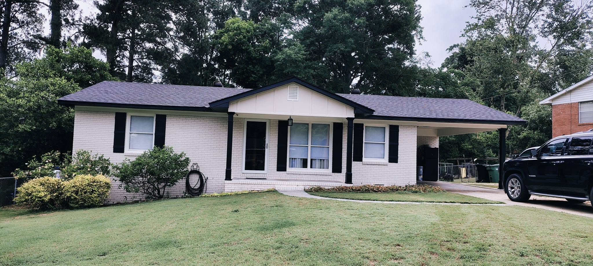 White brick ranch with new dark gray shingle roof and carport